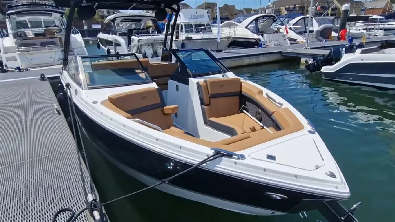 A sleek motorboat with tan seating docked at a marina, surrounded by other boats on a sunny day.